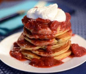 plate with stack of healthy pancakes with healthy strawberry syrup dripping down and topped with greek yogurt
